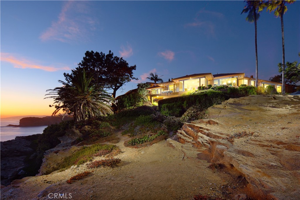 Rarely does a property of this magnitude present itself on the market. A custom ocean-view estate where artistry and nature unite on a blufftop promontory towering over the ocean. A welcoming home that is part luxury, part beauty, and 100% Laguna Beach. Enjoy views that encompass Dana Point, Catalina Island, colorful sunsets, breaking waves, and twinkling evening lights are viewed from most indoor and outdoor living areas at the estate. Located at the end of a private cul-de-sac in South Laguna’s gated Three Arch Bay, the appx. 2.15-acre property encompasses the bluff and part of the beach below. Custom hand-carved mahogany garage doors and a matching entry gate enrich curb appeal, and a private courtyard with Inca Gold natural stone welcomes all with a pool with water feature, electric cover and massaging jets; a built-in  Twin Eagles BBQ bar and Salamangrill and retractable Sunbrella awning; two fire pits and outdoor shower; a full outdoor bath; Bromic heater; and bespoke art from Laguna’s renowned Marlo Bartels. Floor-to-ceiling windows, glass doors, and sliders from Germany’s NanaWall unite exterior spaces with a fabulous interior, where immediate ocean views are experienced upon entry. Main living areas comprise a custom walk-in wet bar with ice-effect glasswork, handmade African movingui cabinetry, a see-through fireplace, a grand dining room that opens to the pool, and a family room with access to an outdoor view deck. The kitchen is as beautiful as it is functional thanks to an island with Brazilian granite top, custom aluminum-finished cabinetry crafted by Bulthaup in Germany, two built-in Miele refrigerators, and a suite of Gaggenau appliances. Blue Bahia and Blue Pearl Granite shine in the primary suite, and select secondary baths reveal Keuco vanities and mirrors. The lower-level theater is accessed by a Garaventa lift and features state-of-the-art A/V equipment. A garage with lift accommodates four cars, a driveway that can fit up three cars, and a Kohler gas backup generator, Lutron lighting, Elan audio, an aluminum roof by Future Roof Systems of Canada, fast water-heating systems, and a 500-gallon whole-home reverse-osmosis system are included.