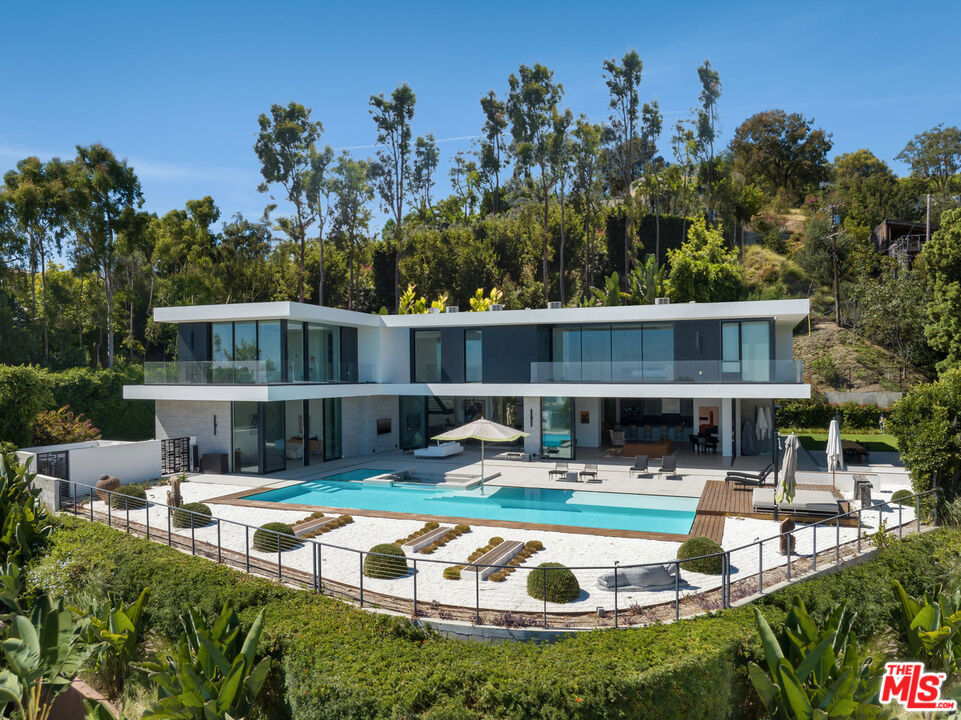 Situated in the heart of Beverly Hills, this extraordinary modern estate is thoughtfully crafted to blur the lines between indoor and outdoor living. The grand two-story entrance, featuring an indoor koi pond, exudes luxury while maintaining a sense of tranquility. Automatic sliding glass doors throughout the home flood each room with light and frame the spectacular views of the city and ocean. The main level is an entertainer's dream, with formal living room, built-in bar, spacious formal dining room, and a gourmet kitchen that flows seamlessly into the family room, making it ideal for gatherings. The whole main level is split up in quadrants which can be enclosed with sliding doors, providing enhanced privacy when needed. A custom made, sound-proof ceiling promotes a sense of tranquility throughout. Two of the seven bedrooms are located on the main floor. Upstairs, the primary suite offers awe-inspiring, unobstructed views, along with his and her bathrooms, expansive walk-in closets, and four additional bedroom suites. The expansive 32,000-square-foot grounds are equally impressive, featuring a zero-edge pool, a lush lawn, a built-in BBQ area perfect for entertaining, and a private putting green. Equipped with home automation systems and security cameras, the estate is located at the end of a private road on a cul-de-sac, ensuring the utmost privacy for the discerning luxury buyer.