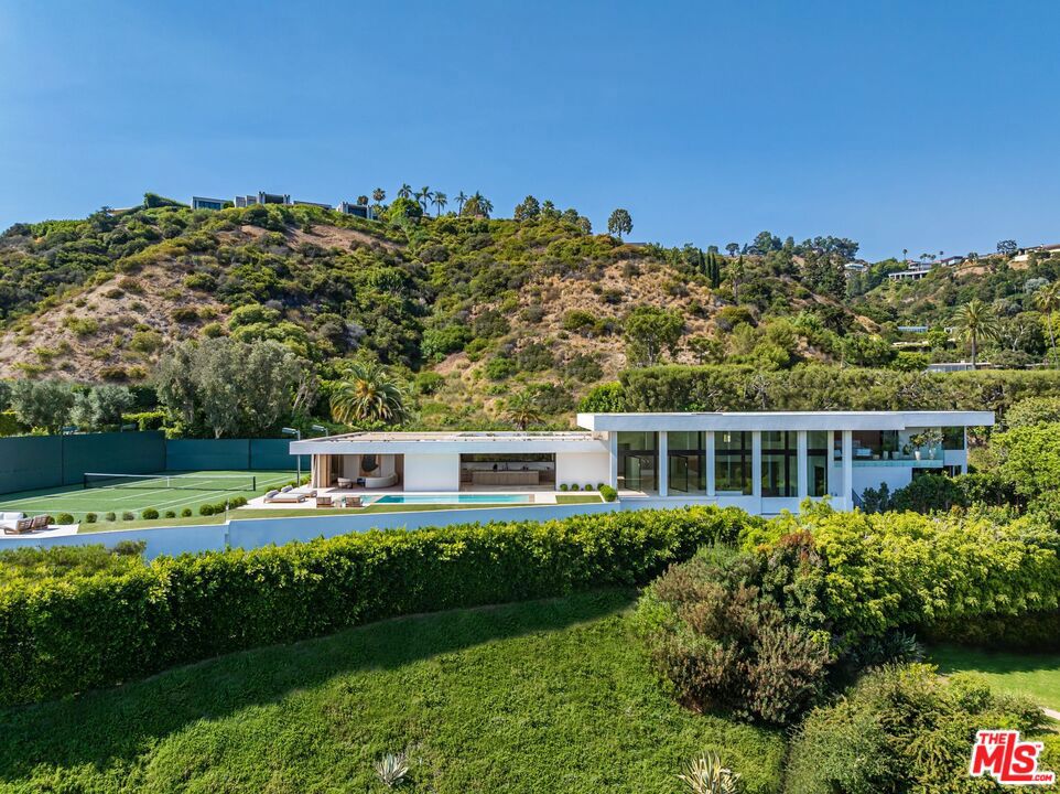The Trousdale Oasis: Trousdale's most exquisite modern interpretation of the greatest era and lifestyle the world has ever known. One-of-a-kind tennis court estate on double lot with explosive views. Designed by the legendary Edward Fickett, FAIA, king of the tennis court estates. The Mid-Century restoration of the ages, a masterpiece born of the finest materials, leading style masters, and most coveted soil on earth. With the longest frontage of any house in Trousdale, it offers unobstructed panoramic views from the city to the ocean and as far the eye can see. Set behind gates and lush 100-year old olive trees to provide the ultimate privacy and security. Open floor plan with 18-foot ceilings, exquisite finishes throughout including fluted Venetian plaster walls and rare blanco Travertine floors mixed with herringbone Fench Oak floors. Oversized family, dining, and living spaces with walls of glass to showcase the views. Arclinea kitchen features Miele appliances, and cabinets by Antonio Lupi. Custom bronze bar with wine cellar. The spacious primary suite has his and her separate bathrooms and walk-in closets, and balcony with views. Pocket glass doors disappear for seamless indoor/outdoor living. Lautner zero-edge swimming pool, spa, outdoor kitchen, fire pits, and multiple seating areas to take in immaculate views. The full-size North/South tennis court has grandfathered-in tennis court lights, which can never be done again in Trousdale. Now is your chance to own a piece of architectural history and luxury in the most exclusive neighborhood with the highest comps in the city, where every detail is designed for the ultimate in elegance and comfort, making this estate a truly once-in-a-lifetime opportunity to live the Beverly Hills dream.