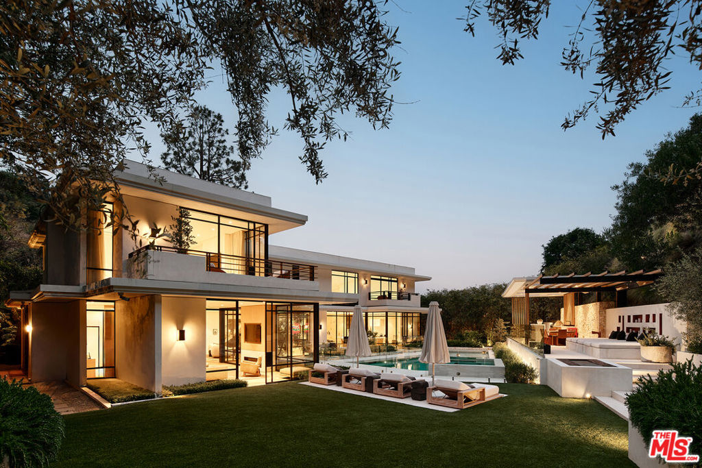 This extraordinary sanctuary, an original modernist masterpiece by renowned architect Charles G. Kanner, has been meticulously updated and expanded for an unparalleled living experience. Set on 2.2 acres behind a private, gated entry and long driveway, this sprawling residence on Heather Road's prestigious eastern cul-de-sac, is enhanced with refined amenities and the latest technologies. Upon entry through captivating architectural canopies, a two-story atrium leads seamlessly into the main living spaces and expansive backyard oasis. Outside, an elevated pergola hosts a full outdoor kitchen, dining, and lounge areas, overlooking a perfectly placed pool and spa, while lush landscaping and treetop city views create a picturesque backdrop. Inside, walls of glass invite abundant natural light, illuminating impeccable interiors that seamlessly fuse indoor and outdoor living. Highlights include a central living room with a custom built-in wet bar, a library/theater room with floor-to-ceiling bookcases, an oversized family room and office with private patio. Perhaps one of the most stunning highlights is the indoor-outdoor courtyard, showcasing a mature Olive tree garden setting thriving beneath a blanket of skylight. The chef's kitchen and breakfast nook, sitting conveniently between all entertaining areas, is a culinary haven - adorned with striking marble and custom oak cabinetry, along with top-of-the-line, hidden appliances. Upstairs, the primary suite is extraordinary - with tranquil treetop and mountain views from all sides and offering a warm, oak-paneled sitting room, private balcony, and a luxurious ensuite bathroom with soaking tub, dual vanity and steam shower, along with 2 spacious walk-in closets. Three additional guest bedrooms looking out over lushly, landscaped grounds, complete the upper level. This breathtaking estate exudes architectural brilliance and contemporary interior sophistication, boasting the highest caliber finishes and meticulous attention to refined details. Set in a prime location within top school districts and close proximity to Beverly Hills' premier attractions, this residence epitomizes refined living at its finest.